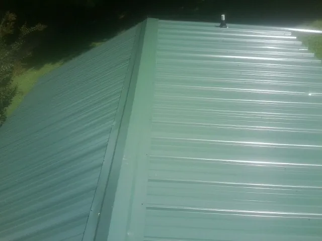 New green metal panels meeting at the ridge of a roof — Flat Roof Repair work by our crew in Weirton