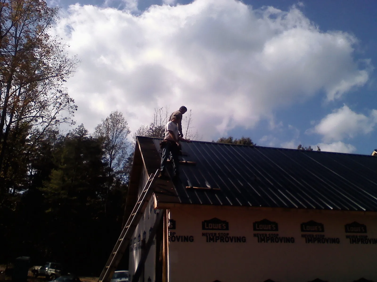 Roofer fastening dark metal panels high against a cloudy sky, from a Roof Inspection job in Weirton