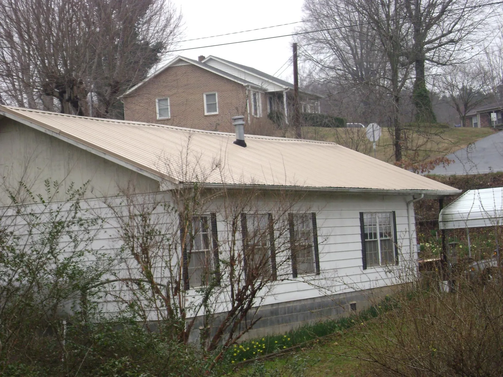 Tan metal roof on a white sided house set into a hillside — Commercial Roofing by Roofing Brothers in Weirton